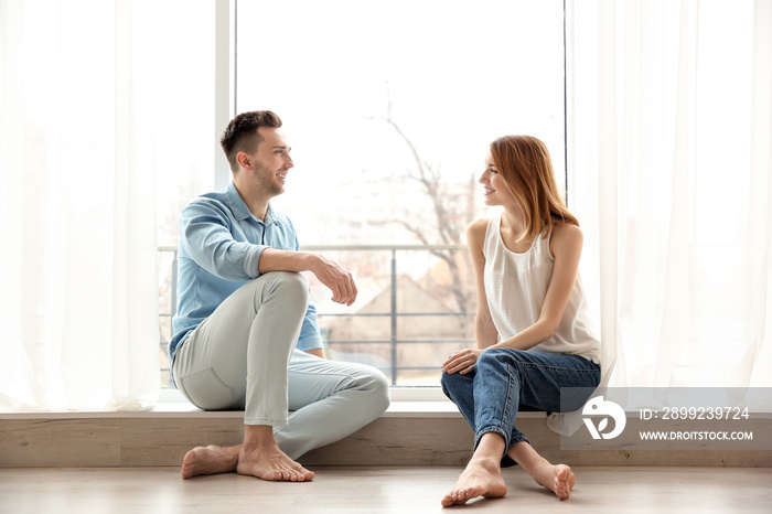 Happy couple sitting on sill near big window