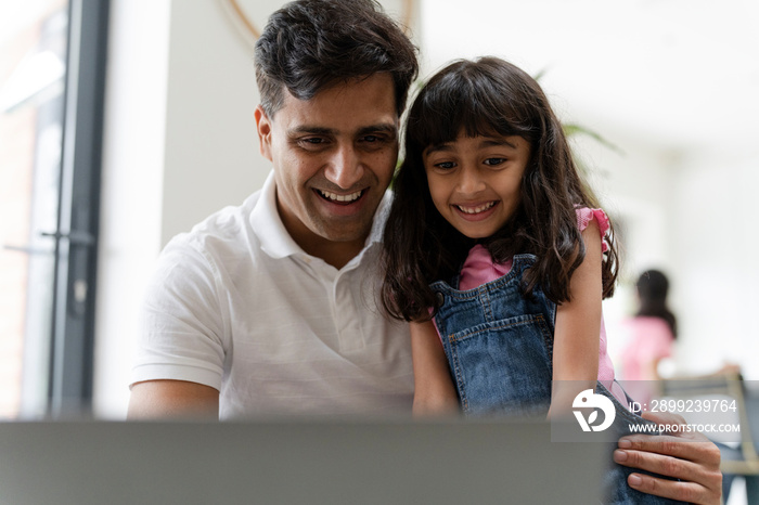 Father sitting with daughter and using laptop