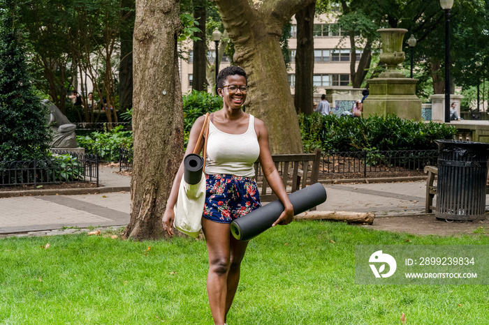 Smiling woman with exercise mat walking in park