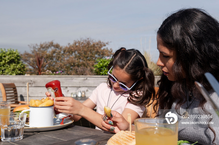 Mother and daughter eating burgers and french fries in outdoor restaurant