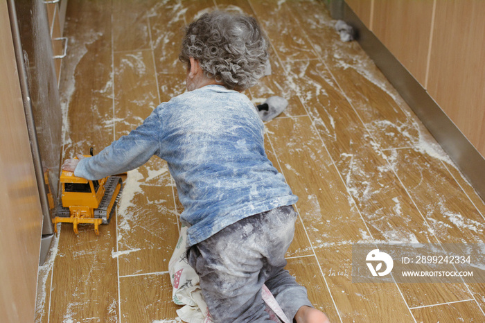 KITCHEN MESSY. LITTLE CHILD PLAYING WITH FLOUR AT THE KITCHEN FLOOR.