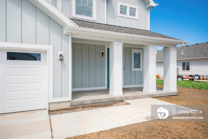 Exterior of a house with light gray board and batten siding and white column posts