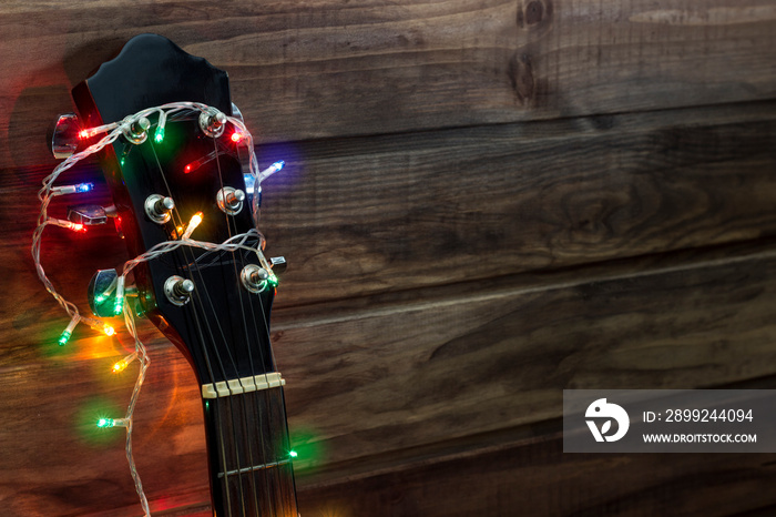 acoustic guitar fretboard in a New Year’s garland, a guitar in a garland under a wooden wall, copy spaсe