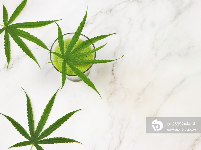 flat lay of cannabis smoothie juice  and marijuana leaves on white marble background.