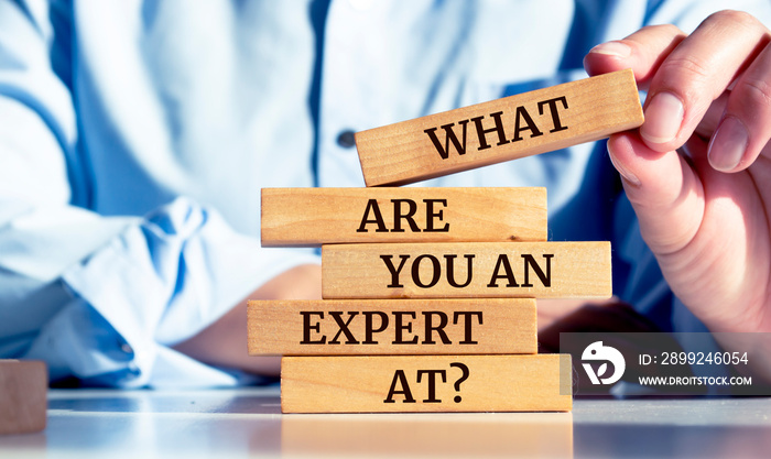 Close up on businessman holding a wooden block with  WHAT ARE YOU AN EXPERT AT?  message