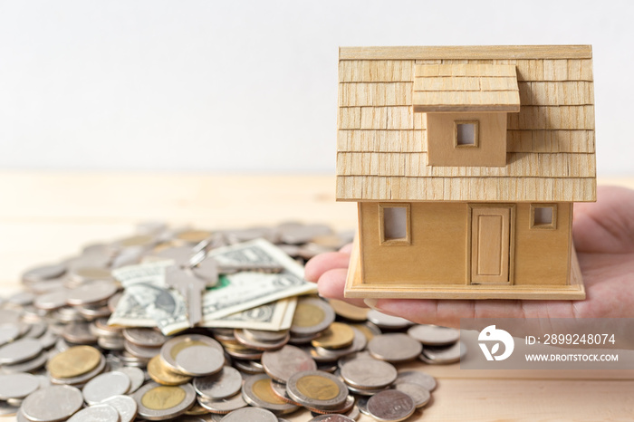 Home loans or real estate concepts, Hand holding wooden house model with key and money cash on wood table over white wall background