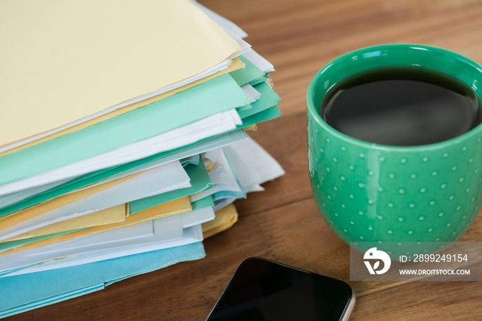 Coffee mug, mobile phone and stacked files on table