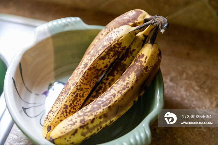 Bunch of very ripe bananas in serving bowl on counter