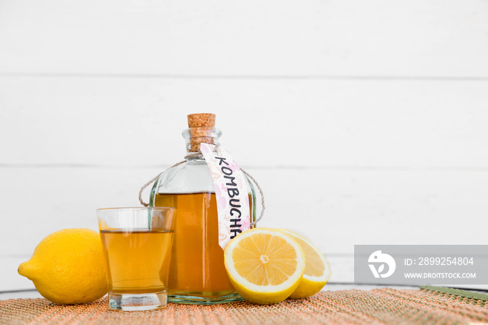 Refreshing filtered kombucha tea in a glass bottle and a glass, with label written kombucha on it, white wooden background.