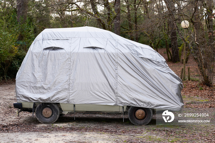 rv camper van car covered with grey protective cover by townhouse for wet weather in parking lot town