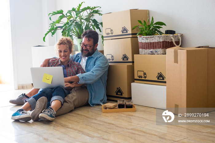 couple of people looking and using together the laptop or computer pc sitting on the ground while are doing a mortgage in a new house moving and packing boxes