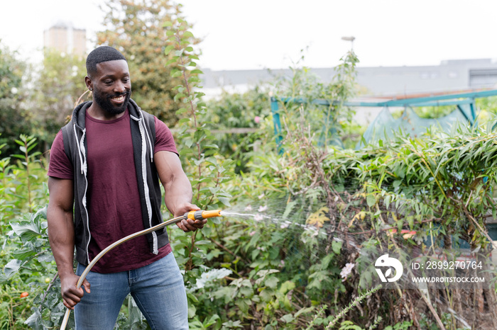 Portrait of smiling man watering vegetables in urban garden