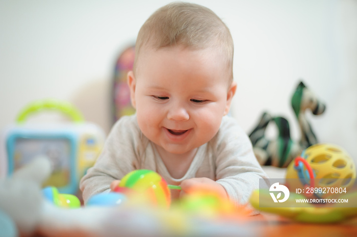 Baby plays with toys. Close-up view of cute baby boy lies on its stomach with an outstretched hand holding a toy and learns about the world around him