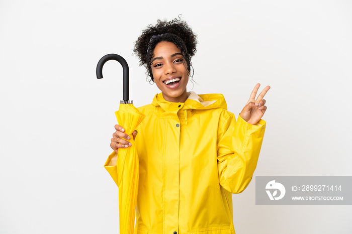 Young woman with rainproof coat and umbrella isolated on white background smiling and showing victory sign