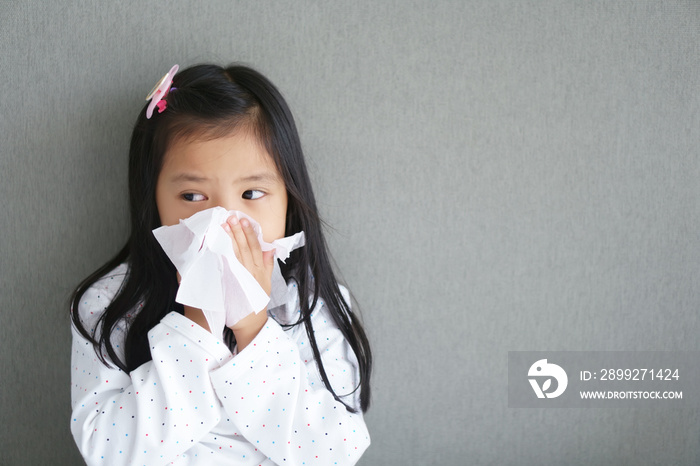 Asian child or kid girl sick and sad with sneezing on nose and cold cough on tissue paper because influenza and weak or virus and bacteria from dust weather and kindergarten school for medical BG