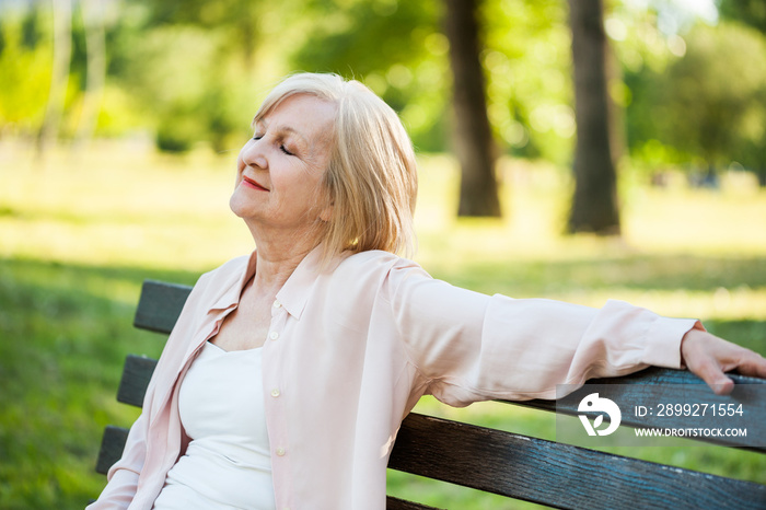 Happy adult woman is sitting in park and enjoying her time.