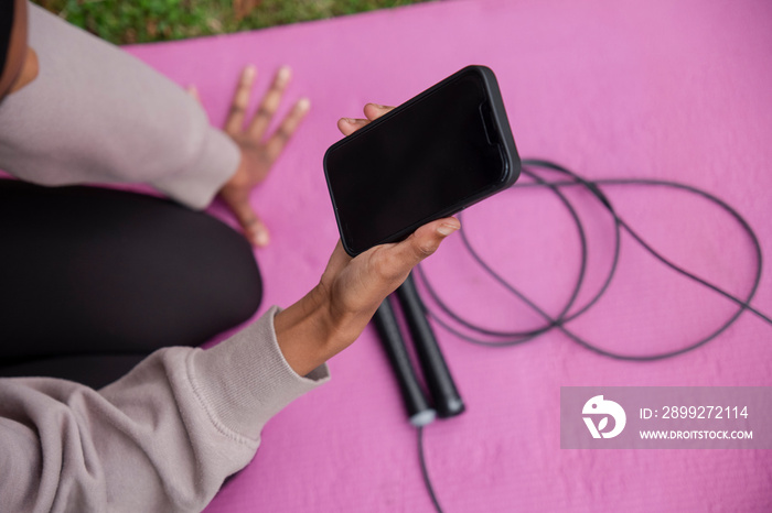 Close-up of woman holding smart phone on pink yoga mat