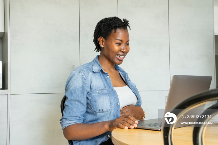 Smiling pregnant woman using laptop in kitchen