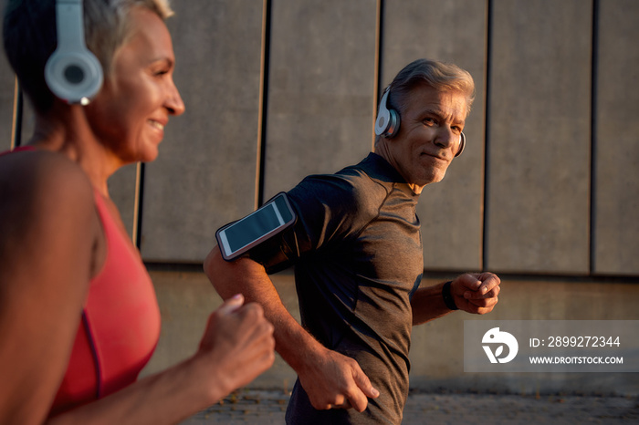 Sport making us closer. Handsome man in headphones running with his wife through the city street in the morning