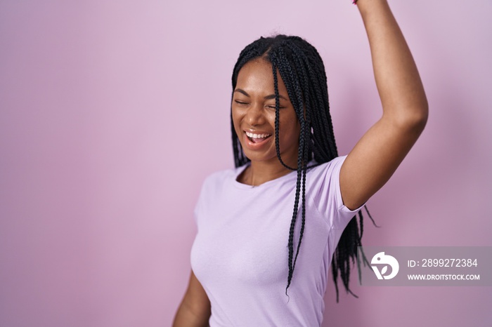 African american woman with braids standing over pink background dancing happy and cheerful, smiling moving casual and confident listening to music