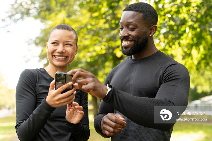 Smiling athletic man and woman looking at smart phone in park