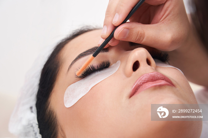 Cosmetologist making eyelash extention and correction using brush