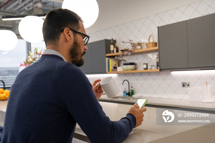 Man using smart phone in office kitchen