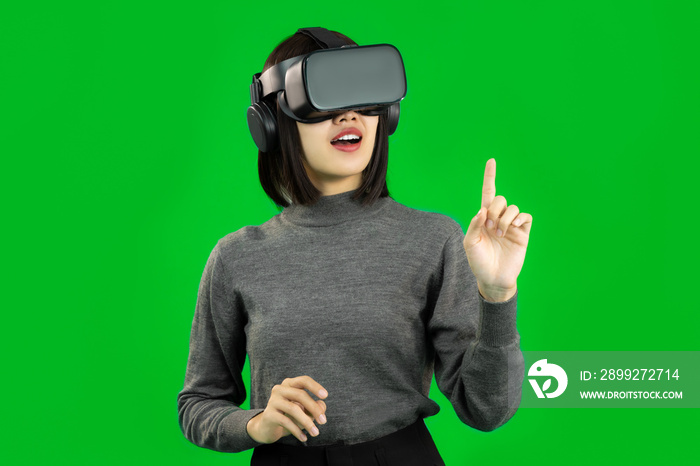 Young Asian woman touching virtual screen, wearing a gray shirt and a VR headset, greenscreen