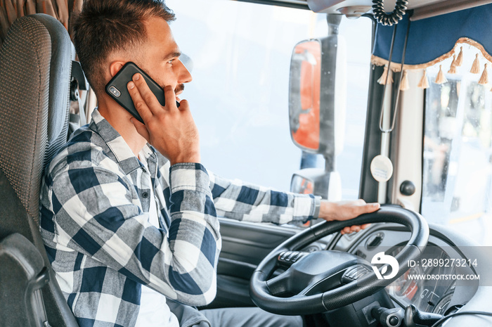 Talking by phone. Young truck driver is with his vehicle at daytime