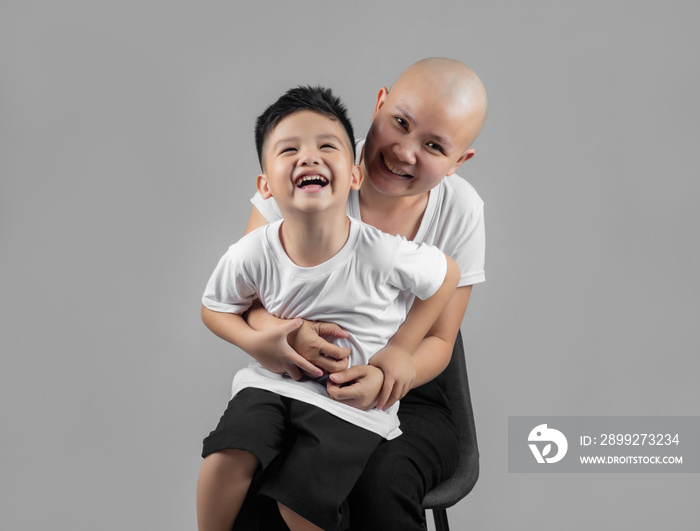 little Asian boy kissing mother, young cancer patient, on the cheek. Cancer and family support concept.