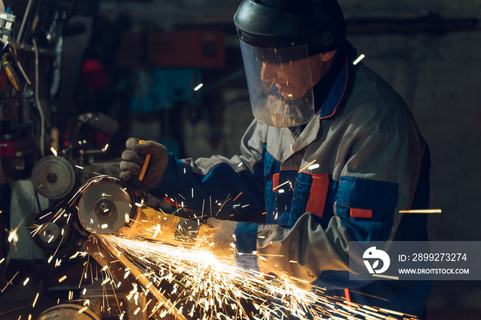 Locksmith in special clothes and goggles works in production. Metal processing with angle grinder. Sparks in metalworking