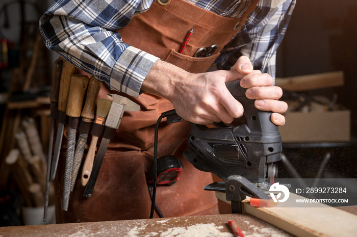 Carpenter is sawing a wood plank with electric jig saw machine in carpentry workshop. Workwood DIY concept. High quality photography.