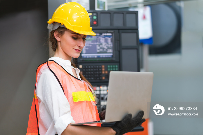 Female Engineer wear face mask ,safety vest and yellow helmet with laptop operating control CNC Machinery at factory Industrial