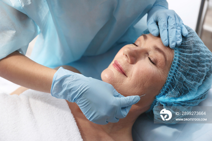 Surgeon operating female patient with scalpel at beauty salon