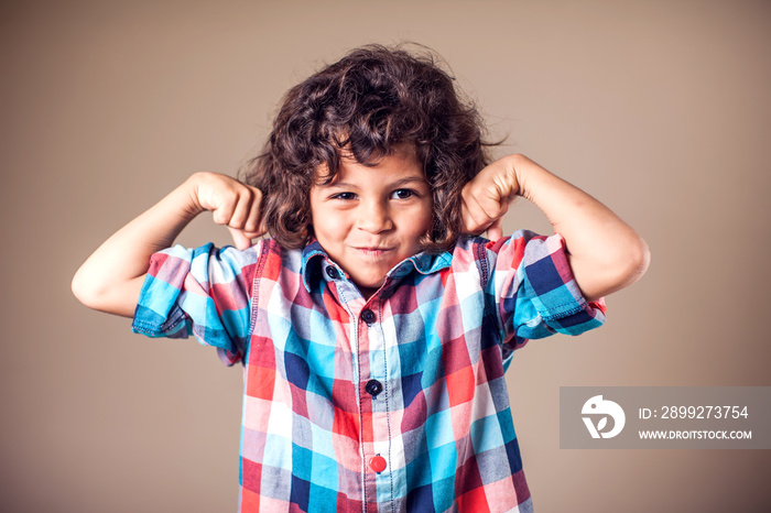 Portrait of a strong kid showing the muscles of his arms