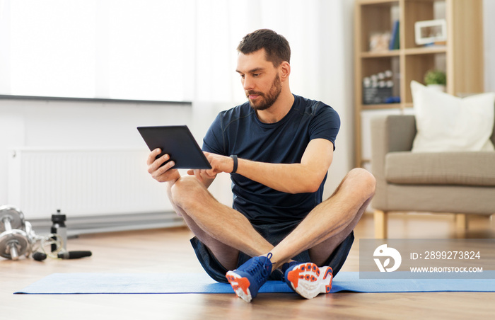 sport, fitness and healthy lifestyle concept - man with tablet computer sitting on exercise mat at home