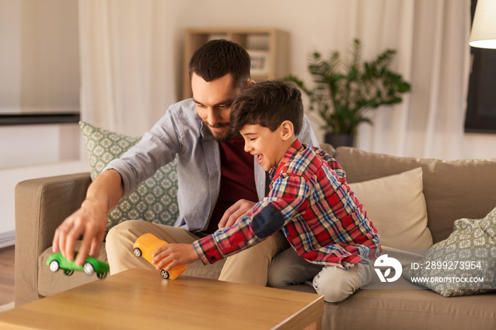 family, fatherhood and people concept - happy father and son playing with toy cars at home