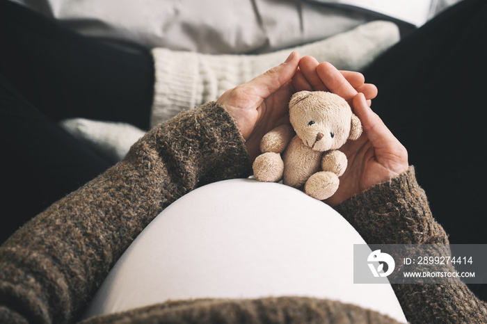 Woman pregnant belly with little teddy toy bear. Concept photo with symbol of many meanings for expectant mother during pregnancy and her unborn baby.