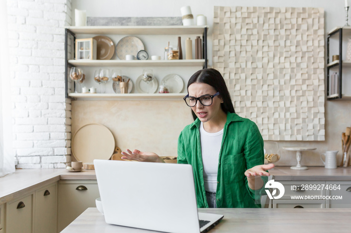 Upset young businesswoman, freelancer works from home He is sitting at the table at home, there is no Internet, the laptop is broken. He spreads his hands angrily.