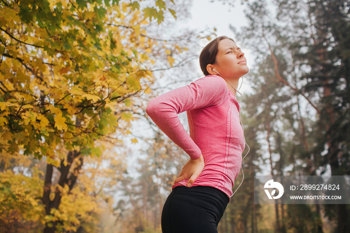 Young woman suffers from pain in back. She stands in autumn park and look up. Woman suffers.