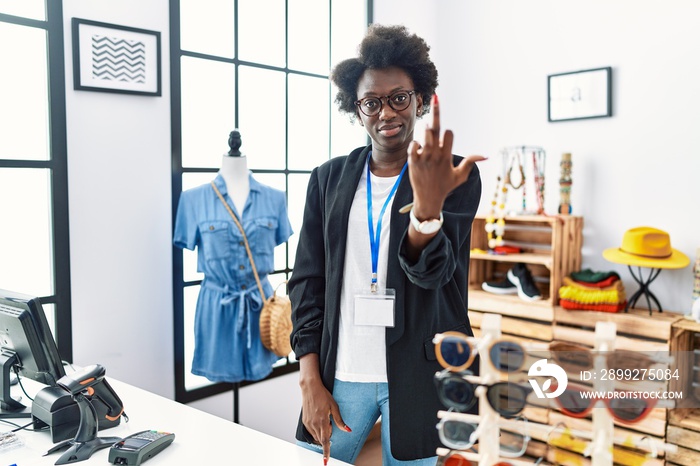 African young woman working as manager at retail boutique showing middle finger, impolite and rude fuck off expression