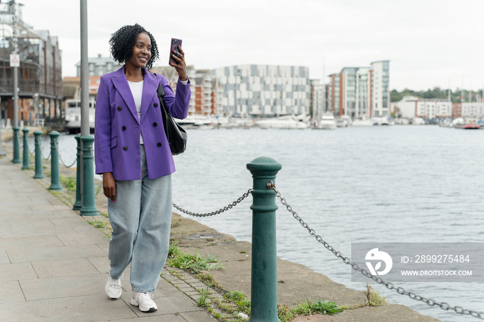 Smiling woman photographing city view with smart phone during walk