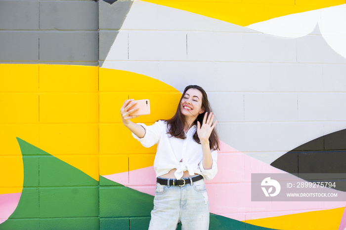 Young woman standing near bright colorful wall using mobile phone, video chatting or calling or texting using social media. Happy lifestyle candid moments of life