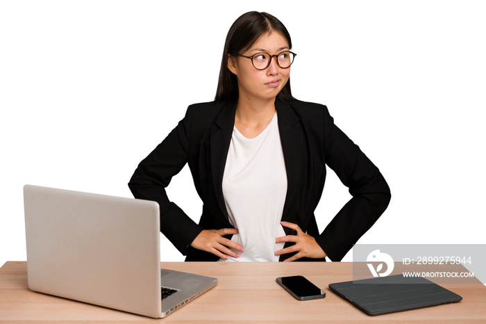 Young business asian woman sitting on a table isolated confused, feels doubtful and unsure.