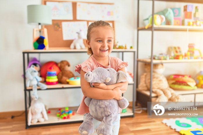 Beautiful blond toddler girl hugging cute stuffed elephant at kindergarten