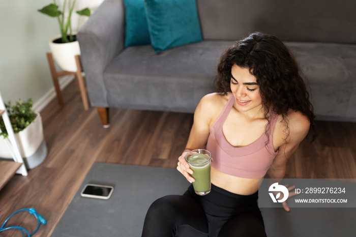 Active young woman about to drink a green clean juice at home