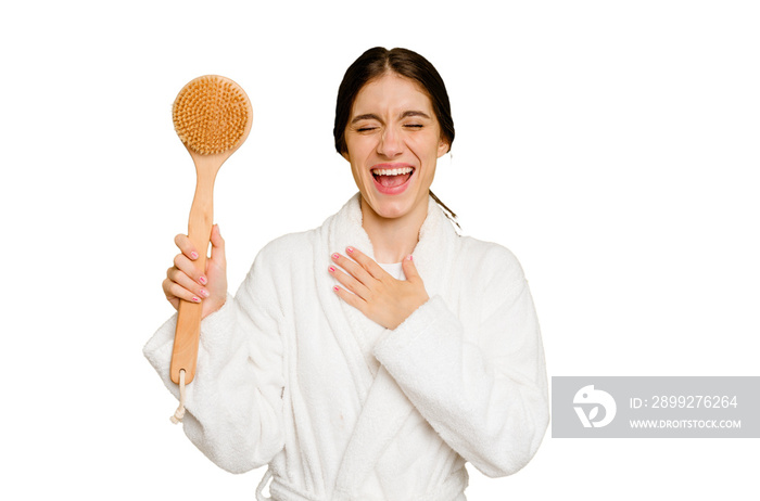 Young caucasian woman holding a shower brush isolated laughs out loudly keeping hand on chest.