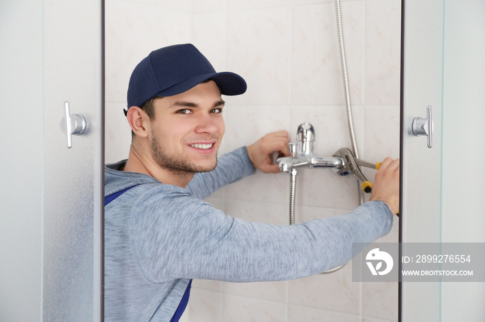 Young handsome plumber fixing faucet in shower stall