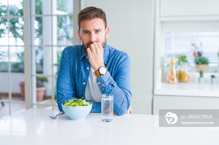 Handsome man eating fresh healthy salad looking stressed and nervous with hands on mouth biting nails. Anxiety problem.