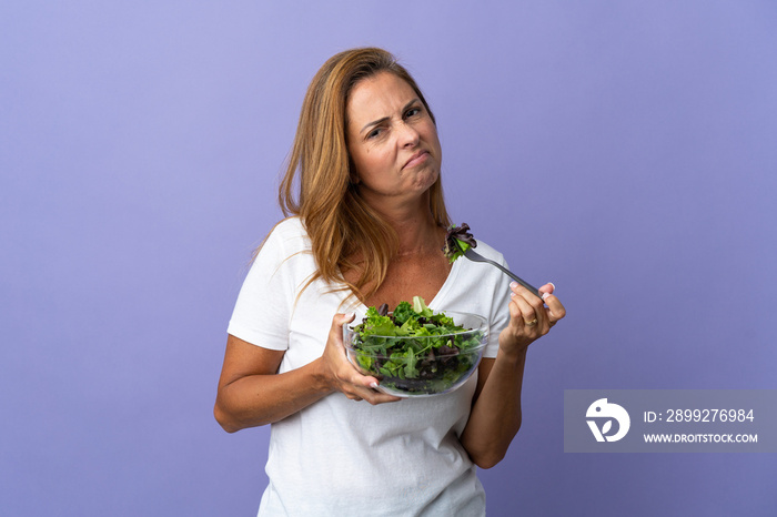 Middle age brazilian woman isolated on purple background holding a bowl of salad with sad expression